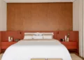 A mesa de cabeceira traz funcionalidade e personalidade ao quarto. Nesta casa projetada pela Paiva e Passarini Arquitetura, a dupla de mesinhas integra a cabeceira de marcenaria e se destaca do painel que veste a parede | Foto: Xavier Neto