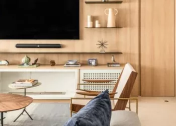 Na sala de estar desse apartamento, o arquiteto Bruno Moraes lançou mão da porta mimetizada para ocultar o acesso ao corredor que dá acesso à ala íntima. Discreta, ela assumiu também o papel de extensão do painel da TV | Projeto BMA Studio | Foto: Guilherme Pucci