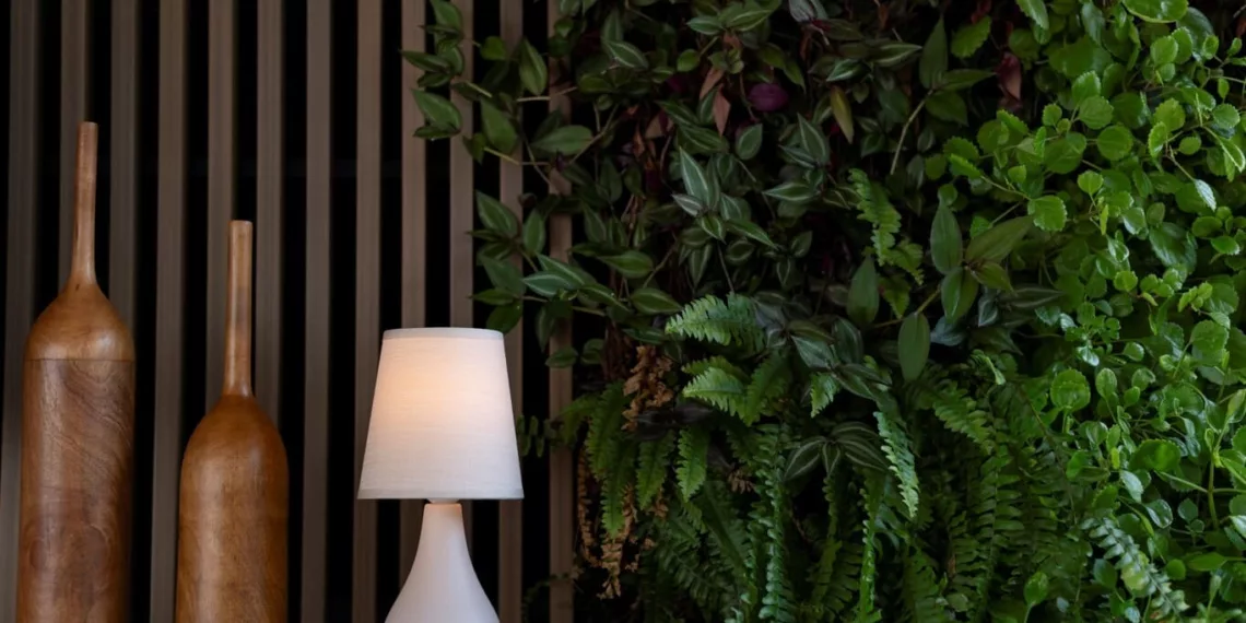 A parede verde é protagonista do estar e cria uma sensação de relaxamento. O painel e os adornos de madeira complementam a atmosfera natural juntamente com o abajur em cerâmica da Yamamura Collection / Projeto do escritório Degradê Arquitetura e foto de Emerson Rodrigues