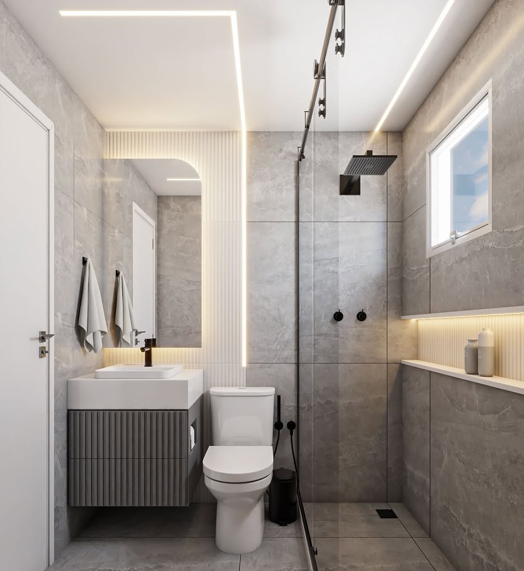 Banheiro moderno em tons de cinza com gabinete ripado, iluminação LED embutida, metais pretos e nicho decorativo sob a janela. Ambientes claros e sofisticados com design clean.