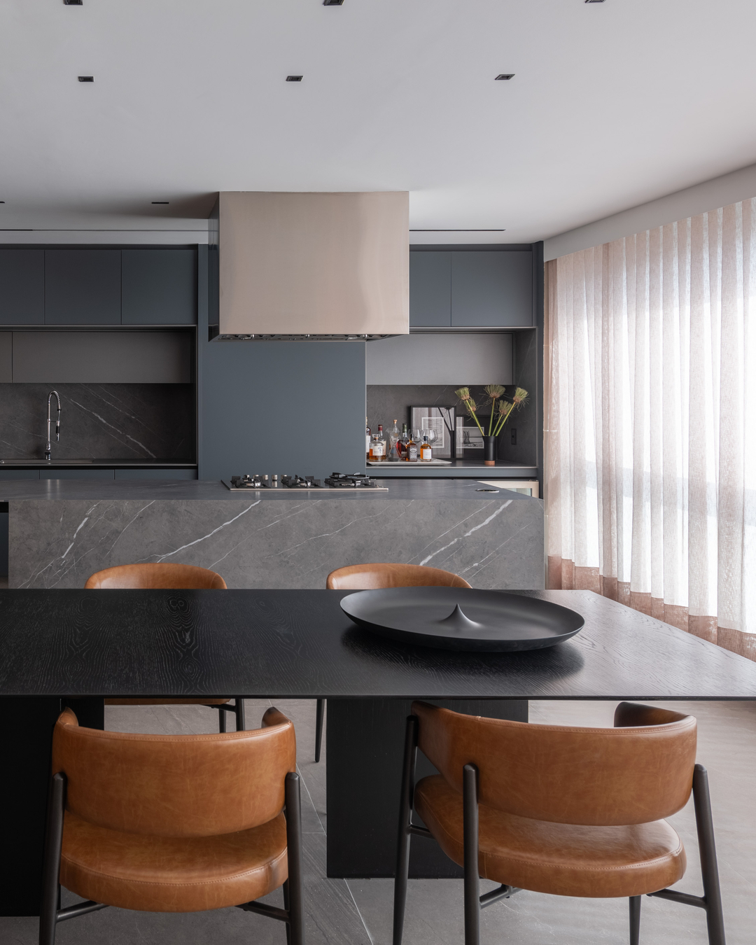 Cozinha integrada com sala de jantar, ilha em pedra e cadeiras de couro caramelo em projeto moderno.