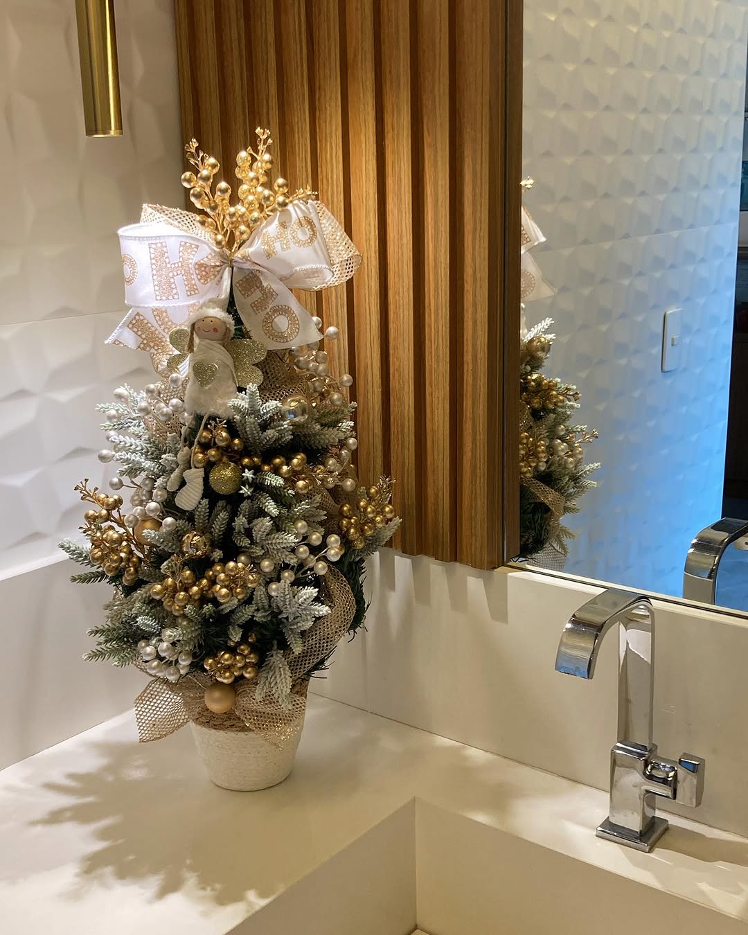 Mini árvore de Natal decorada com dourado e branco em banheiro sofisticado, com fita personalizada e enfeites perolados.