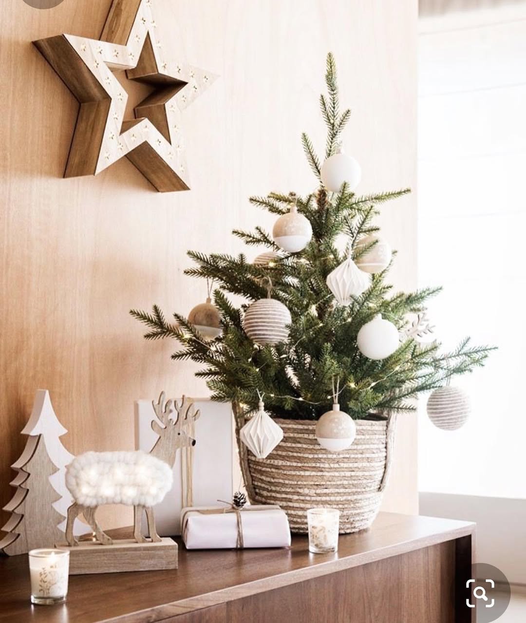 Mini árvore de Natal natural com bolas brancas e cesto de palha sobre aparador em ambiente escandinavo com luz suave.