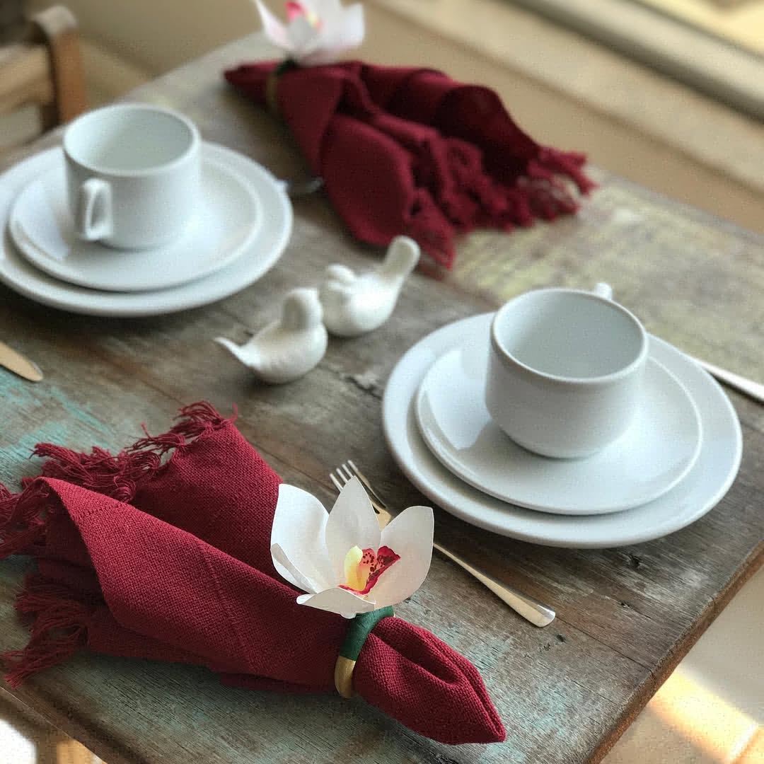 Guardanapo vinho com porta-guardanapo de flor branca em mesa rústica com louça branca.