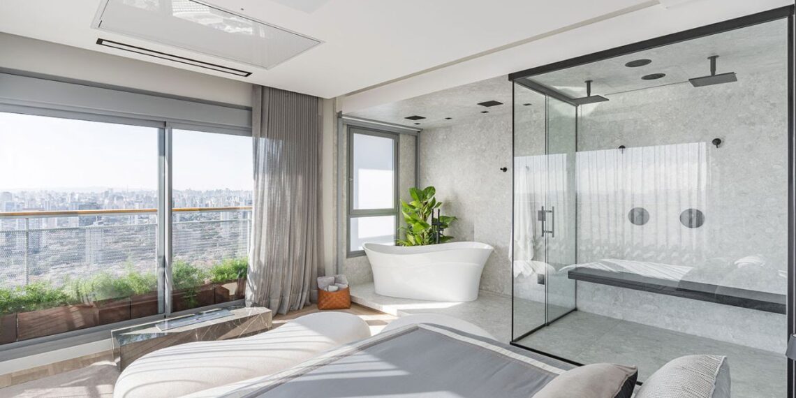 Um dos pedidos do morador para a Spaço Interior foi aproveitar o skyline de São Paulo não só na área social como na suíte master. Assim, integrado ao quarto, com vista para a Ponte Estaiada, está a sala de banho com banheira de imersão, box translucido, duchas duplas e até banco – tudo pensado para trazer os benefícios terapêuticos de uma sauna | Foto: Kadu Lopes