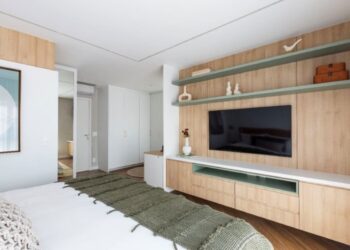 A parede em frente à cama pode seguir diversas linhas decorativas, recebendo pinturas, revestimentos ou painéis de marcenaria. O cuidado está em combinar o material e não competir com a TV | Projeto: Mari Milani | Foto: Mariana Camargo