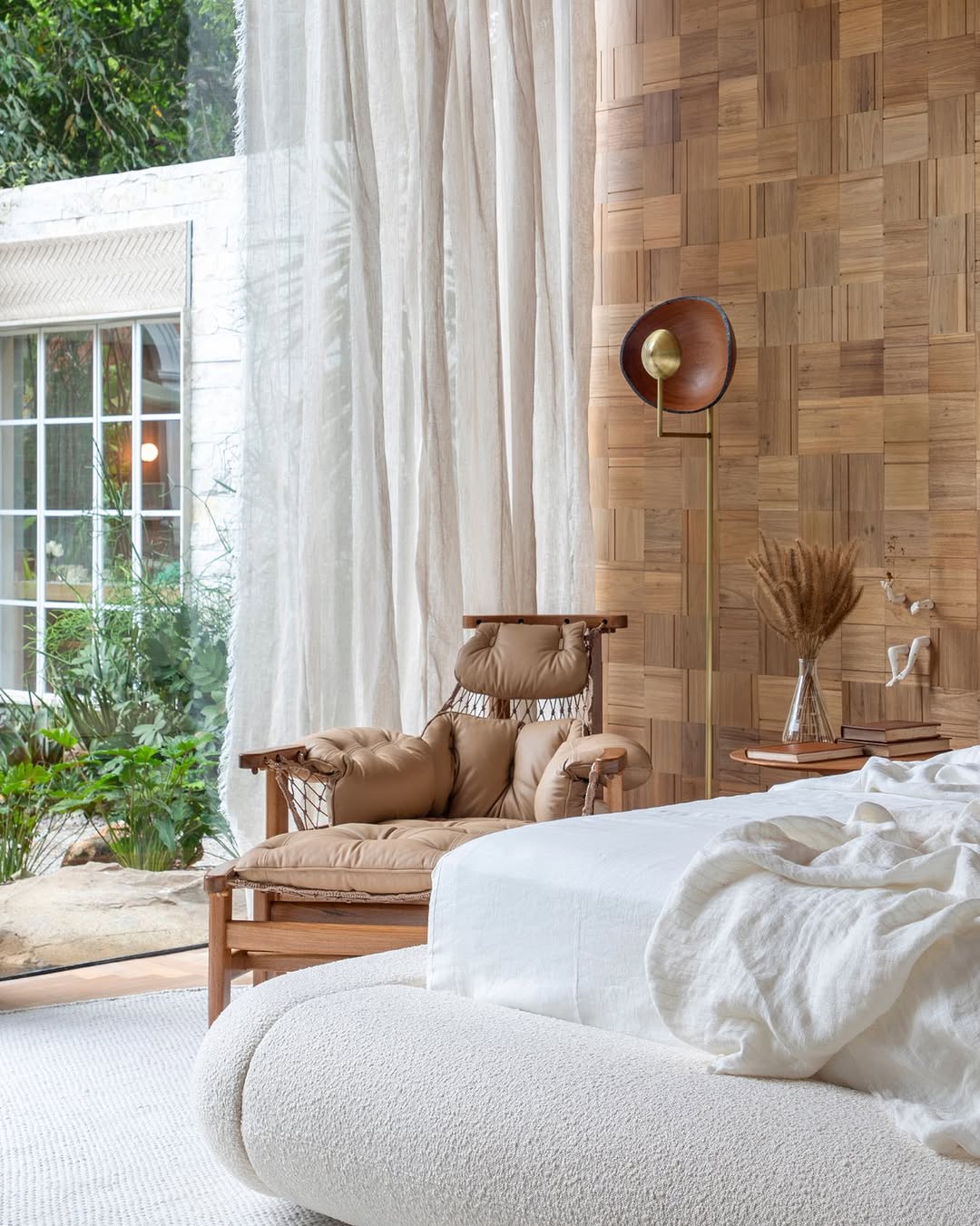 Poltrona Jangada em quarto iluminado, com cortinas de linho e parede de madeira ripada.