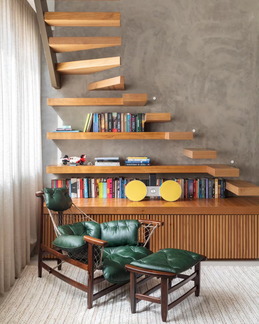 Poltrona Jangada com couro verde em canto de leitura com escada suspensa e estante de madeira.