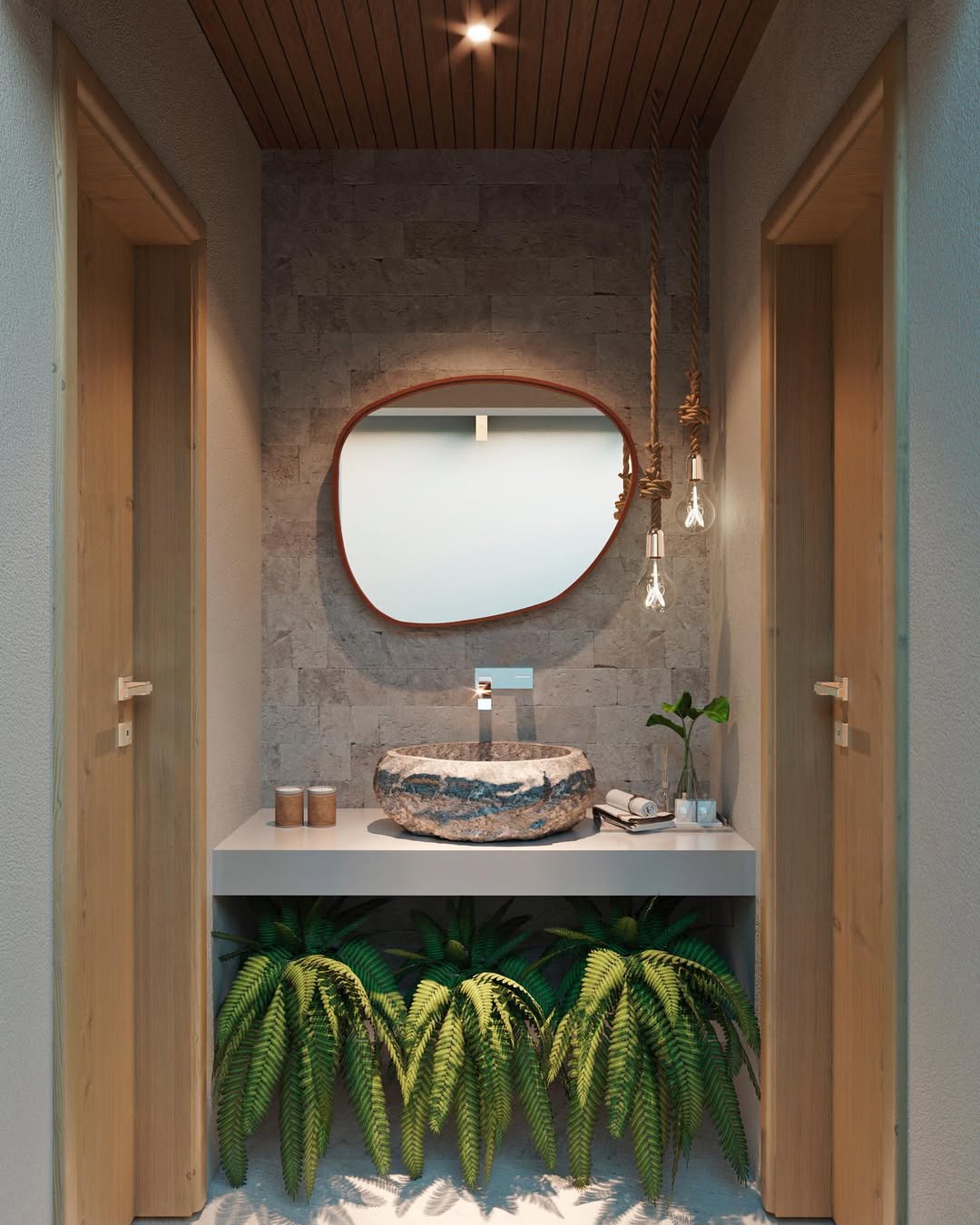 Lavabo rústico com cuba de pedra sobre bancada minimalista, espelho orgânico com moldura em madeira e jardim de samambaias sob a pia, iluminado por pendentes em corda e teto ripado em madeira.