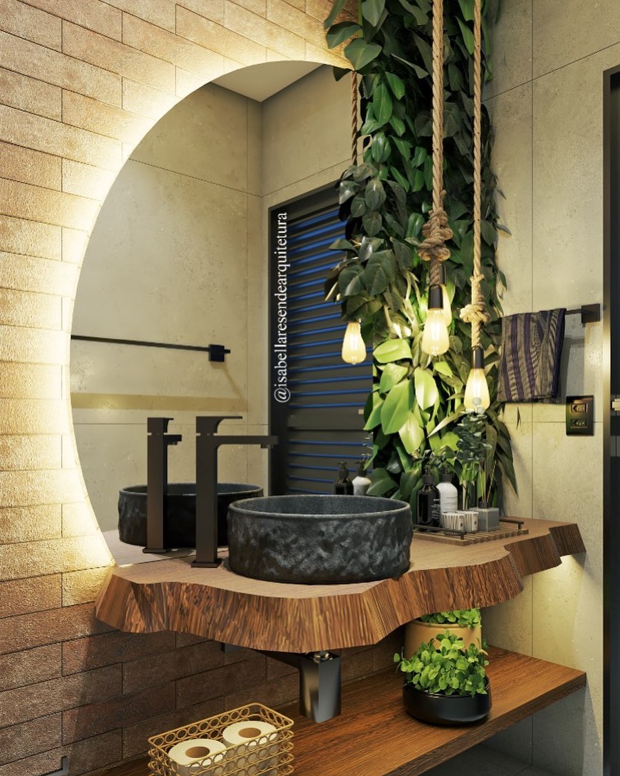 Lavabo rústico com bancada de madeira bruta, cuba de pedra escura, pendentes com cordas grossas e jardim vertical ao lado do espelho iluminado, criando ambiente natural e sofisticado.