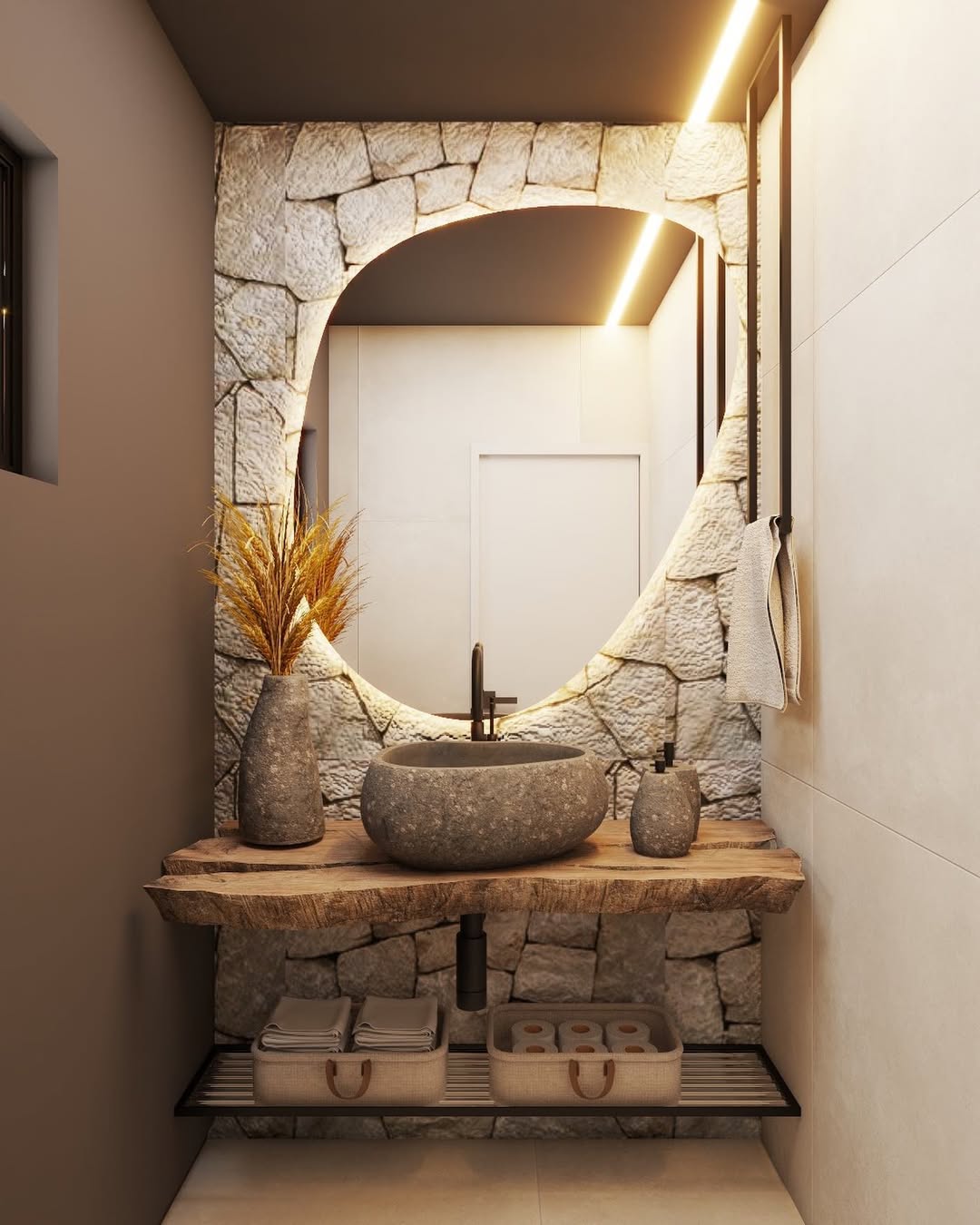 Lavabo rústico com parede de pedras irregulares, espelho orgânico iluminado por LED, bancada de madeira natural e cuba de pedra redonda, com cestos decorativos no nicho inferior.