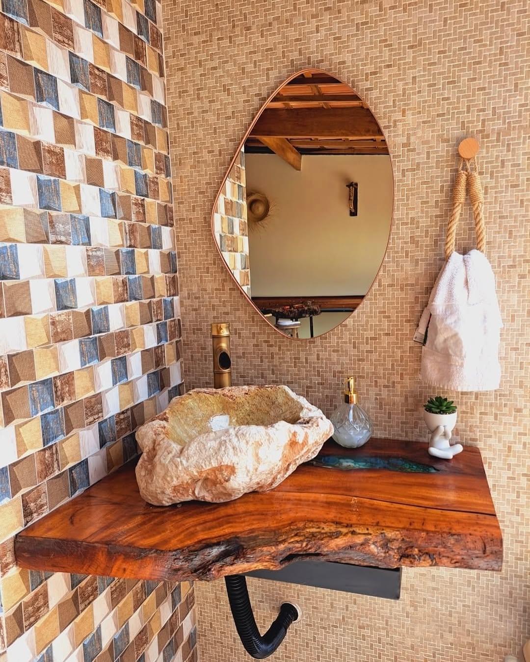 Lavabo com bancada de madeira viva de bordas irregulares, cuba esculpida em pedra e espelho orgânico sobre parede texturizada, criando efeito rústico artesanal.