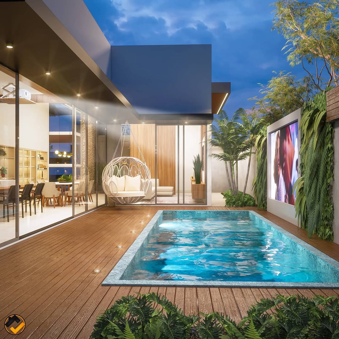 Piscina com churrasqueira integrada em área externa noturna, com deck de madeira, iluminação embutida, área gourmet envidraçada, balanço suspenso, paisagismo tropical e layout contemporâneo voltado ao lazer.
