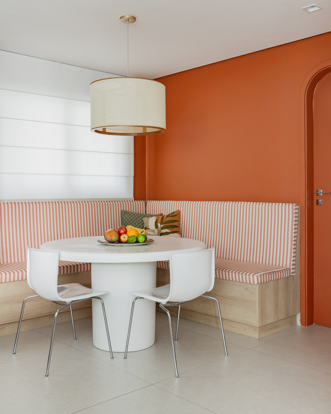 Canto alemão com parede terracota, mesa redonda branca e estofado listrado em um projeto que prioriza conforto e convivência no duplex dos Jardins.