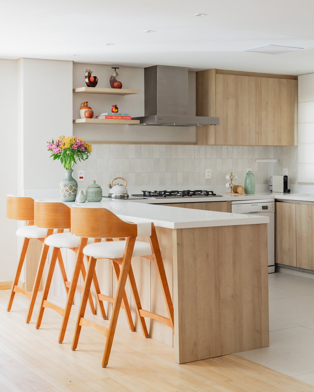 Cozinha integrada com bancada em L, banquetas de madeira clara e armários planejados, unindo elegância e praticidade para o dia a dia familiar.