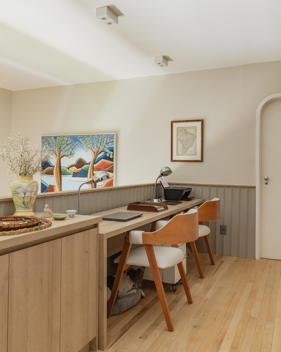 Home office no mezanino com bancada dupla, cadeiras de madeira clara e ambiente acolhedor que também abriga os pets da família.