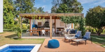 Área externa com piscina, deck amadeirado e espreguiçadeiras integradas à área gourmet em casa revitalizada no interior de São Paulo.