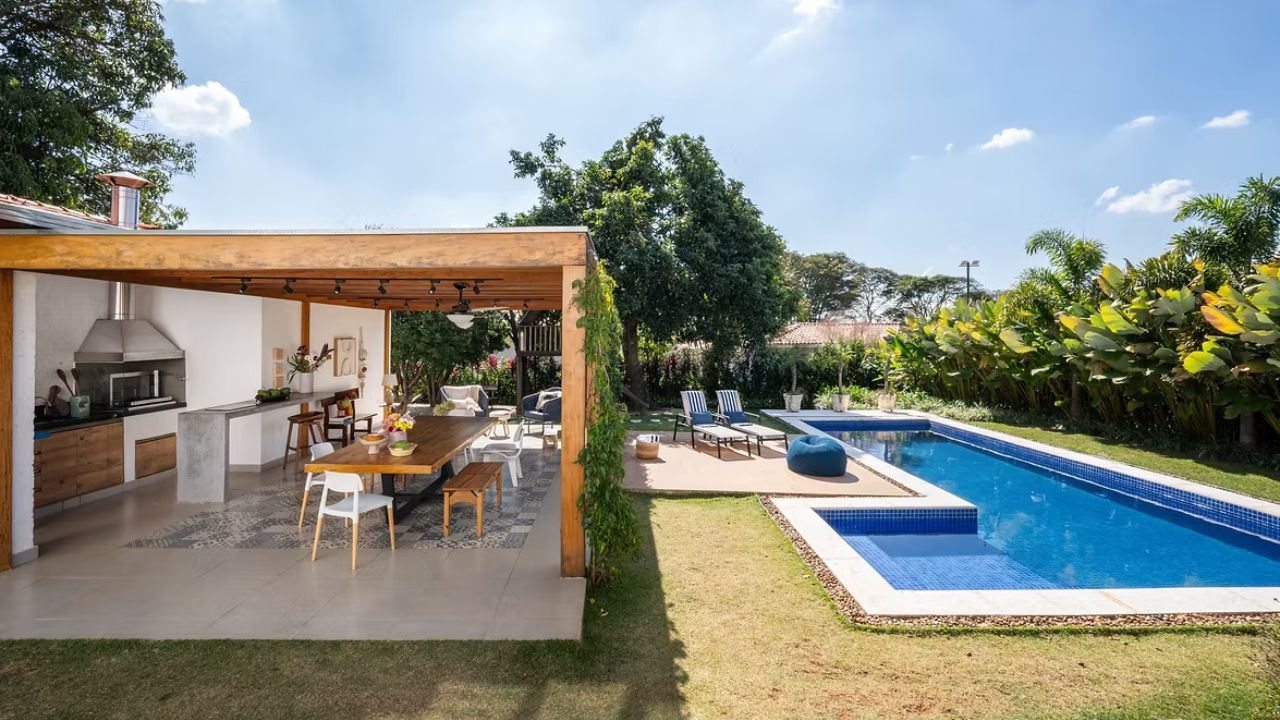 Área gourmet com pergolado de madeira integrada à piscina e jardim em projeto de revitalização residencial.