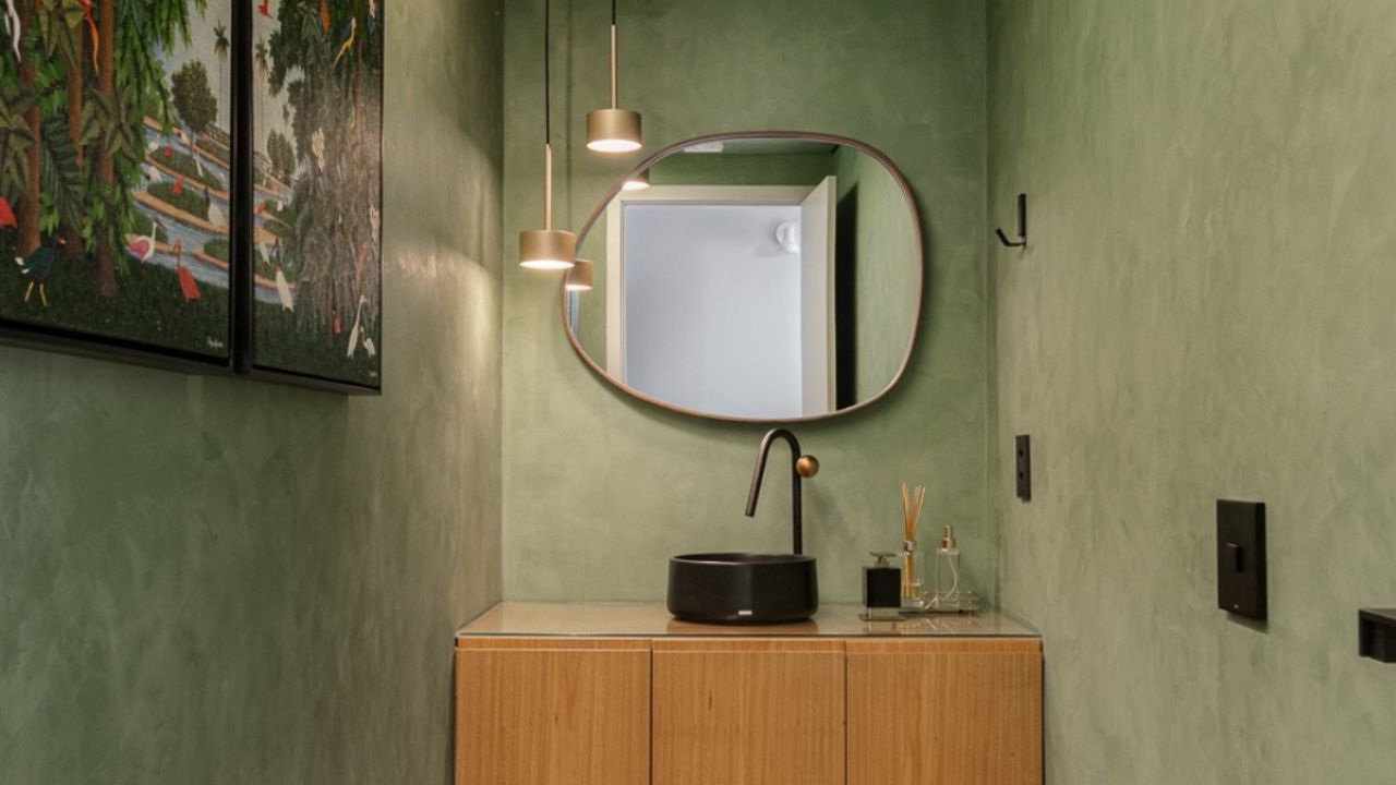 Lavabo com paredes verdes, bancada de madeira e cuba preta, uso sofisticado do verde na decoração de banheiro.