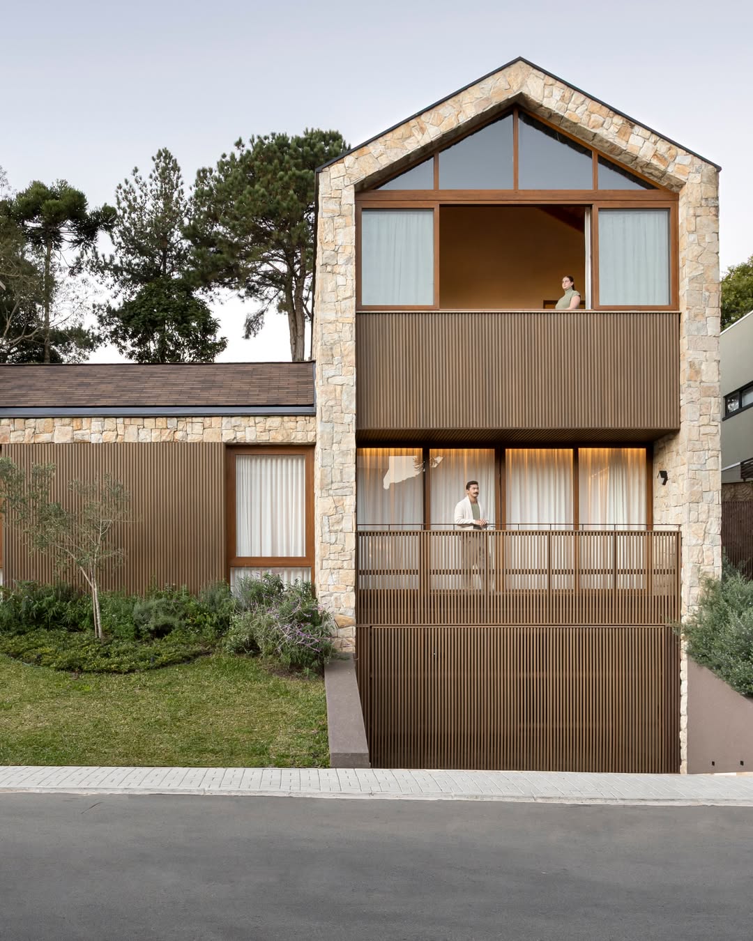 Fachada de casa em Curitiba com revestimento de pedra natural, ripado de madeira e telhado em duas águas — projeto do Estudio Elmor em Santa Felicidade.