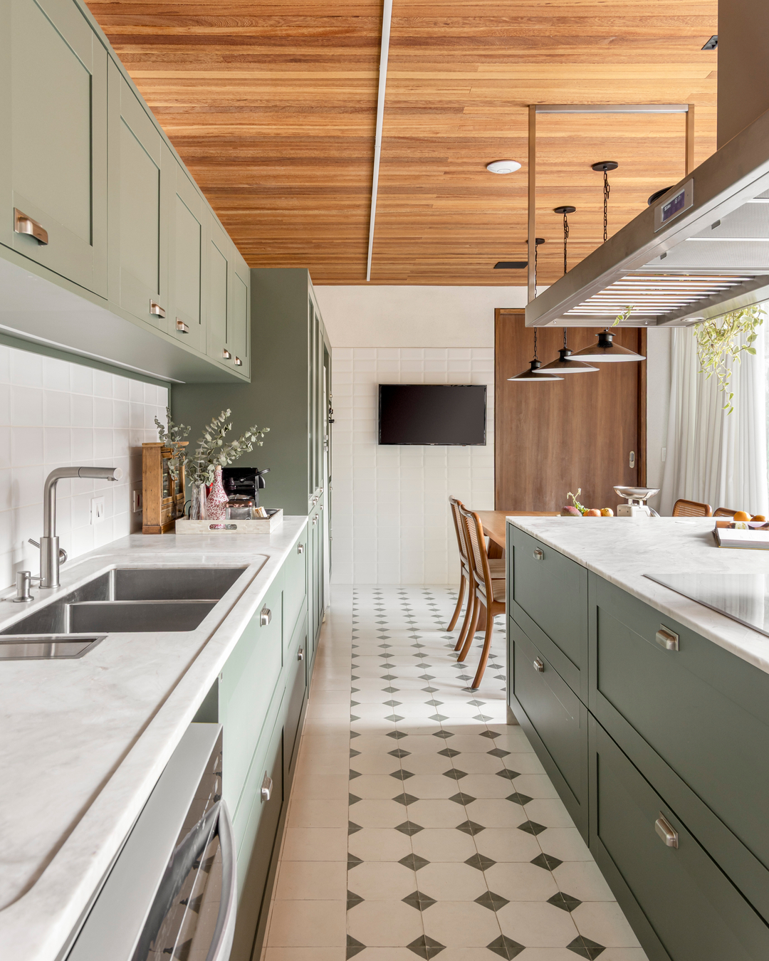
Cozinha com armários verde-musgo, bancada de mármore branco, forro de madeira Peroba Mica e piso de ladrilho hidráulico geométrico — residência do Estudio Elmor em Curitiba.