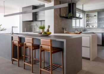 Nesse projeto realizado pelo arquiteto Raphael Wittmann, a bancada, executada em lâmina ultracompacta, atende a cozinha como espaço para as refeições, além de estender-se para a área gourmet. Para os assentos, três charmosas banquetas Ada, em couro, assinadas pelo Estudiobola | Projeto Rawi Arquitetura + Design | Foto: Rafael Renzo