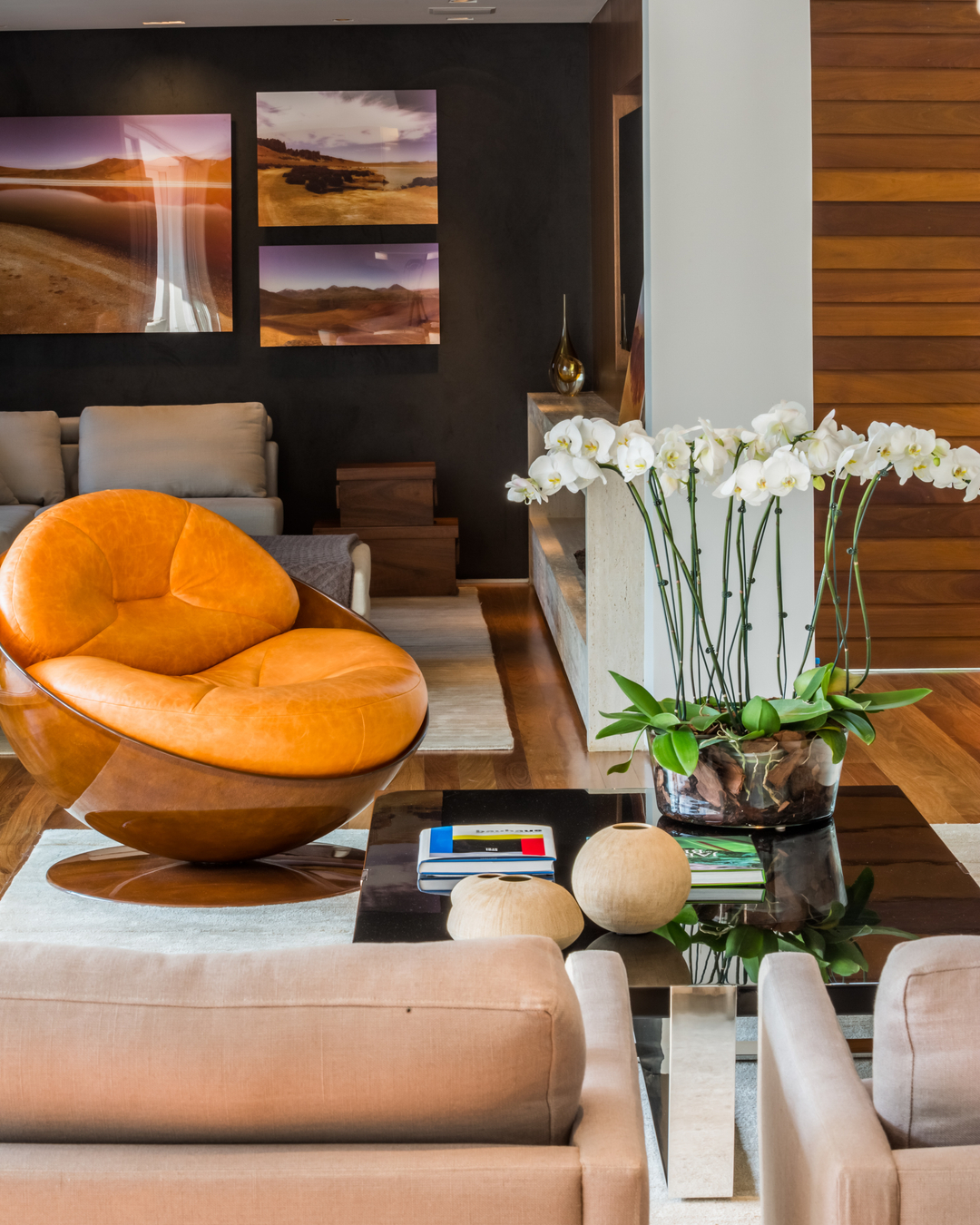 Living com poltrona Esfera de couro laranja de Ricardo Fasanello, mesa de centro preta com orquídeas brancas e painéis de madeira, em residência contemporânea em São Paulo