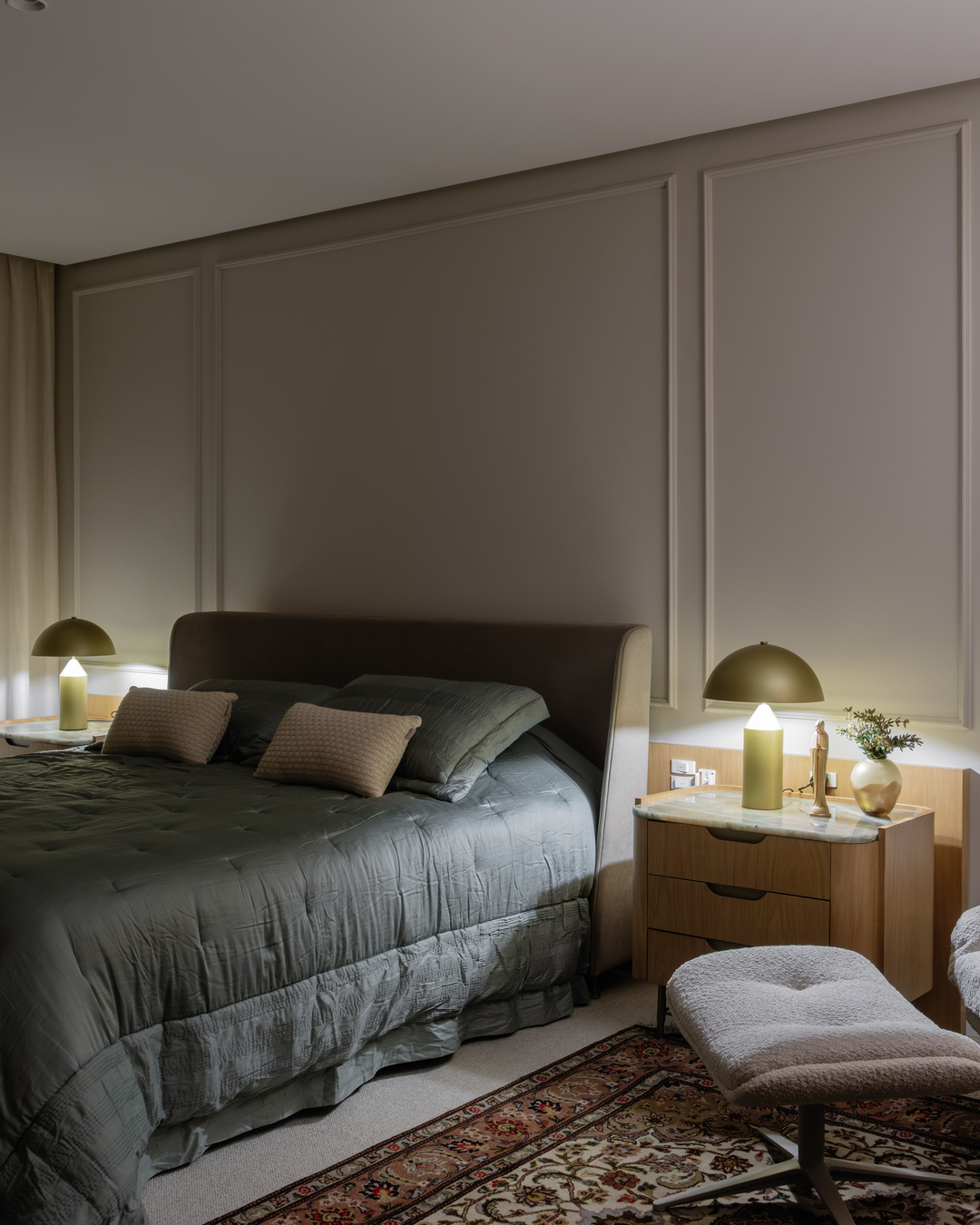 Quarto com cabeceira estofada, iluminação indireta e tapete clássico.