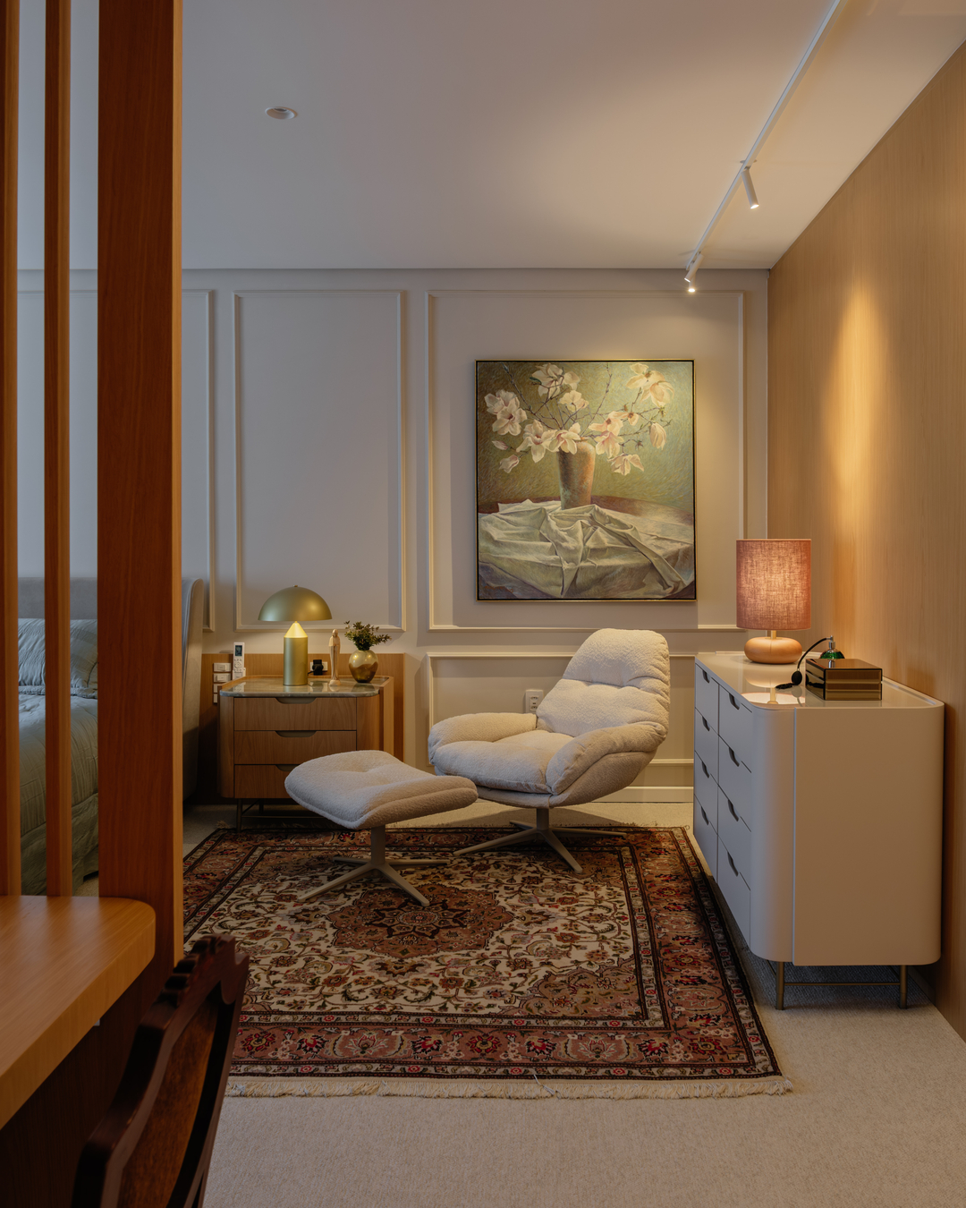 Canto com poltrona reclinável, quadro floral e marcenaria em madeira clara.