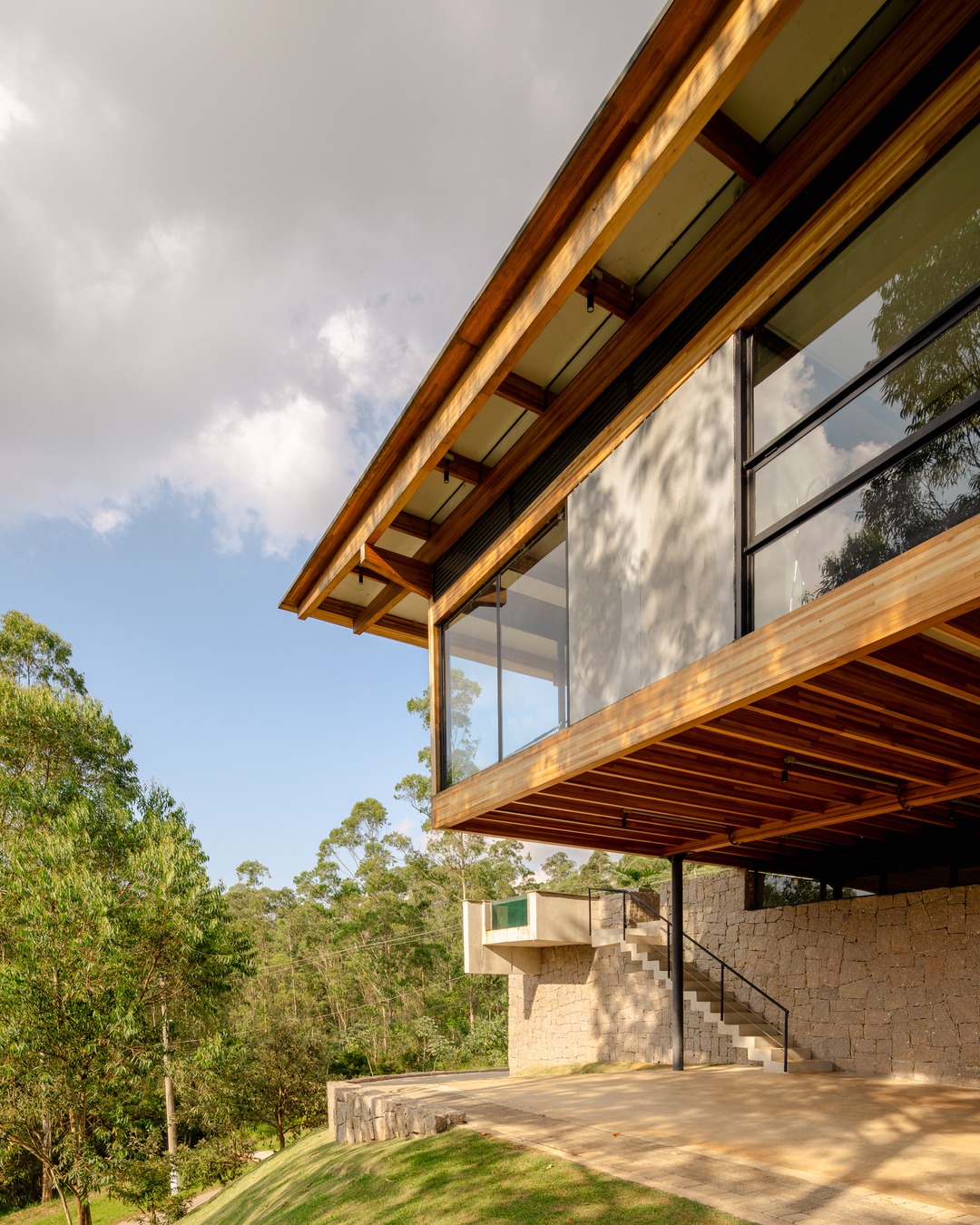 Casa CLV em Cajamar com estrutura de madeira laminada colada elevada sobre pilotis metálicos e base em pedra natural, projeto Cornetta Arquitetura