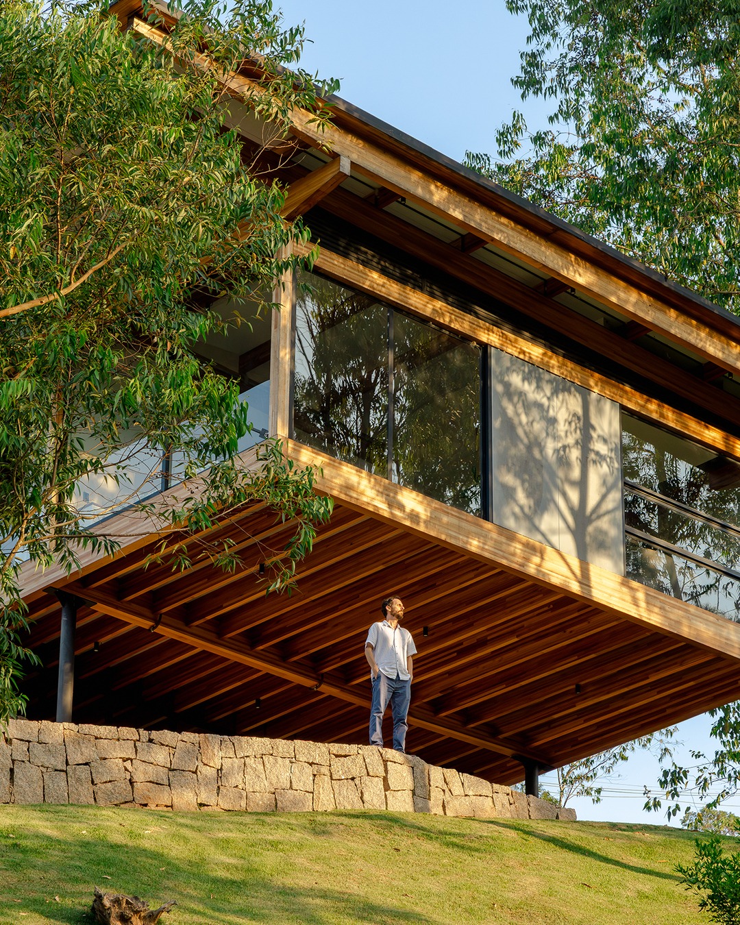 Exterior da Casa CLV com cobertura de madeira laminada colada, pilotis metálicos e paisagismo natural ao redor, Cornetta Arquitetura, Cajamar SP
