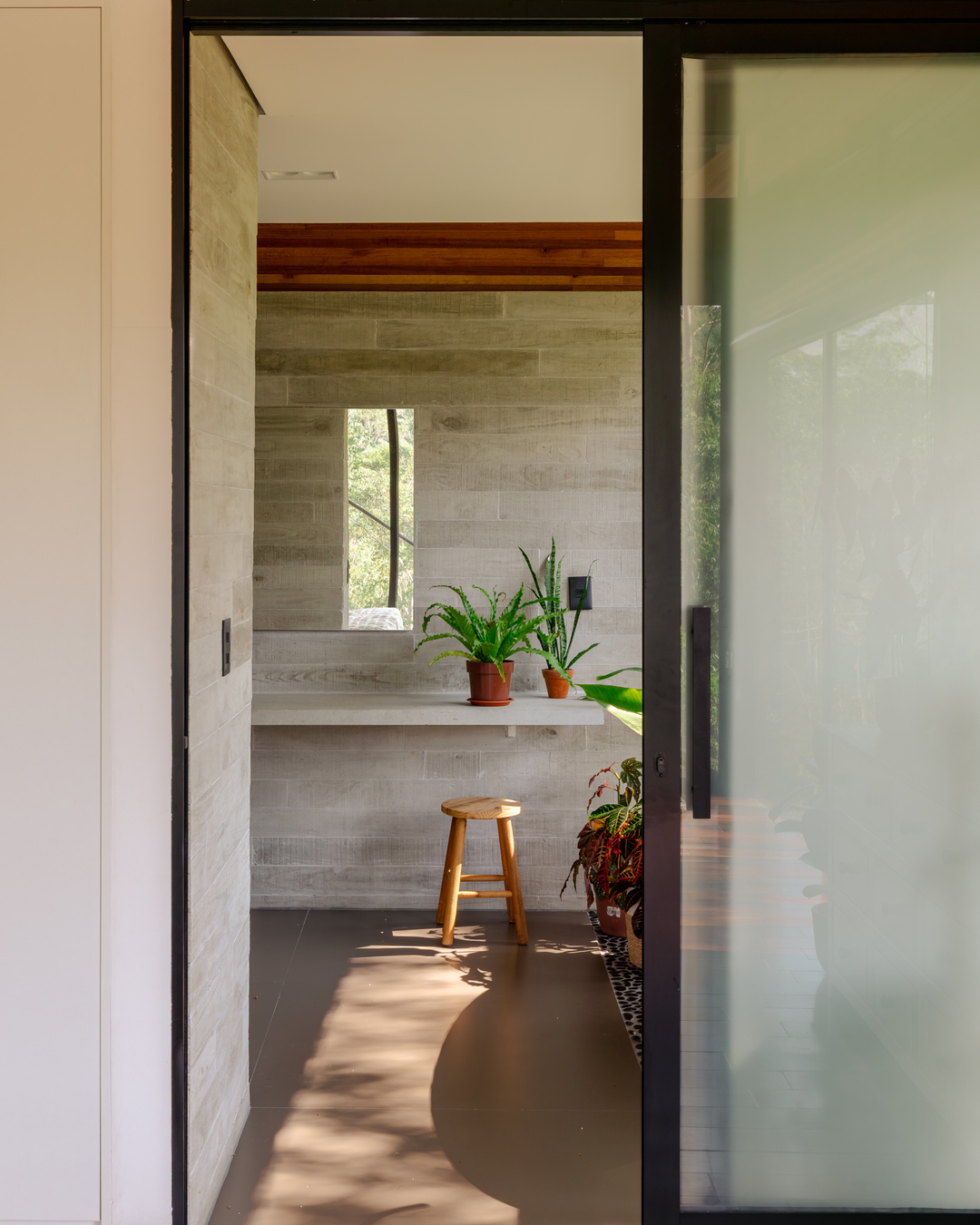 Hall interno da Casa CLV com paredes de concreto aparente texturizado, vigas de madeira laminada colada no teto e plantas ornamentais, Cornetta Arquitetura