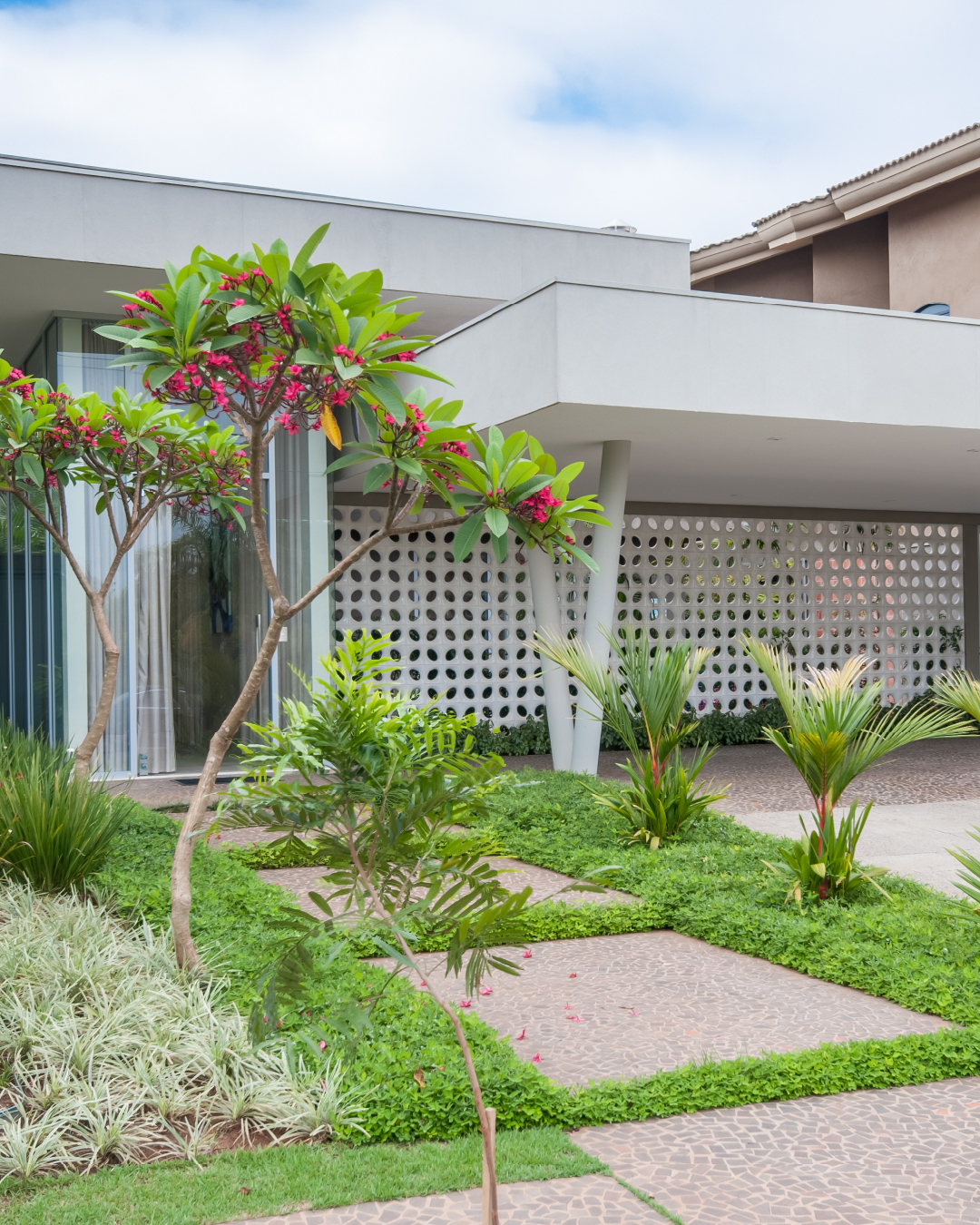 Fachada moderna com cobogó branco, jardim tropical e piso em mosaico português, destacando ventilação natural e arquitetura brasileira.