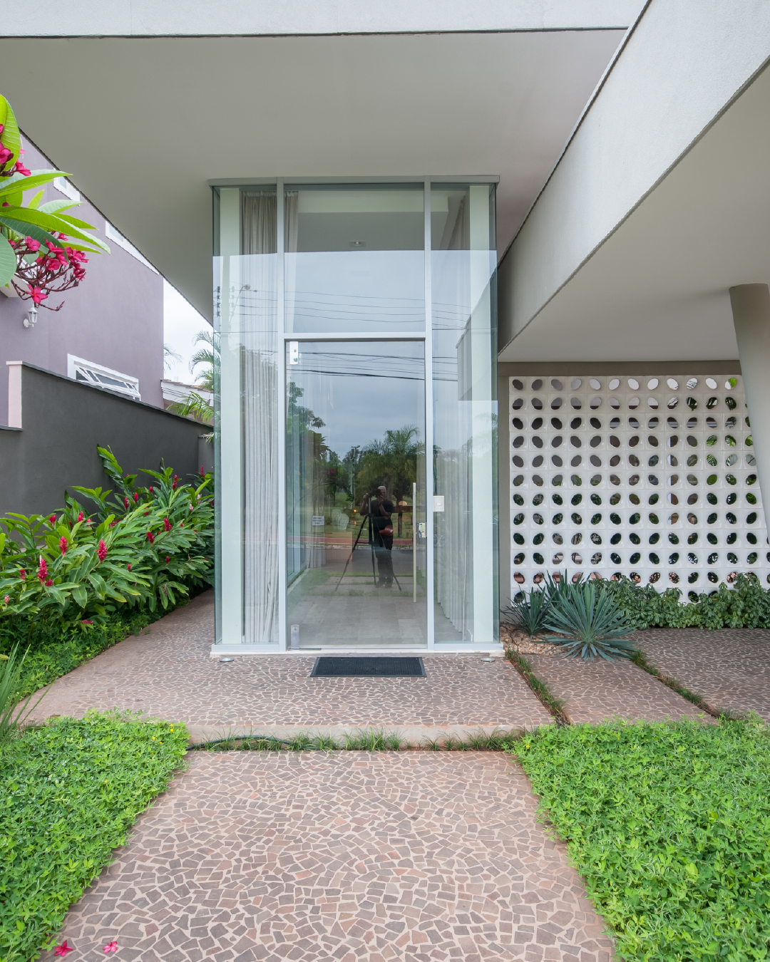 Entrada residencial com porta de vidro e cobogó branco ao fundo, integrando ventilação natural e design moderno brasileiro.