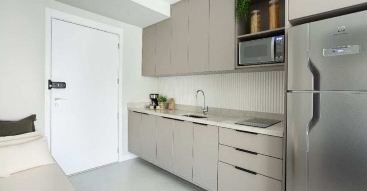 Em imóveis com metragem reduzida, como no caso dos studios, é possível garantir uma cozinha otimizada: nesse projeto do escritório ResiliArt Arquitetura, a marcenaria envolve o espaço da cozinha que começa desde a porta de entrada. É preciso definir o que é realmente necessário: o cooktop de duas bocas atende com eficácia e não houve a instalação do forno, haja vista não se fazia fundamental na rotina do morador | FOTO: Kelly Queiroz