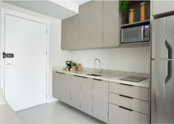 Em imóveis com metragem reduzida, como no caso dos studios, é possível garantir uma cozinha otimizada: nesse projeto do escritório ResiliArt Arquitetura, a marcenaria envolve o espaço da cozinha que começa desde a porta de entrada. É preciso definir o que é realmente necessário: o cooktop de duas bocas atende com eficácia e não houve a instalação do forno, haja vista não se fazia fundamental na rotina do morador | FOTO: Kelly Queiroz