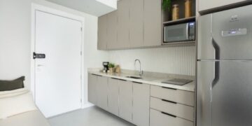 Em imóveis com metragem reduzida, como no caso dos studios, é possível garantir uma cozinha otimizada: nesse projeto do escritório ResiliArt Arquitetura, a marcenaria envolve o espaço da cozinha que começa desde a porta de entrada. É preciso definir o que é realmente necessário: o cooktop de duas bocas atende com eficácia e não houve a instalação do forno, haja vista não se fazia fundamental na rotina do morador | FOTO: Kelly Queiroz