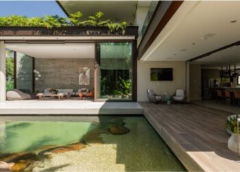 No projeto desta residência, com a assinatura da arquiteta Patricia Penna, a piscina lago se integra ao paisagismo de forma orgânica com suas bordas, pedras naturais e madeira. Atrás dele, o grande painel de vidro, com 7,20 m, se abre por completo, diluindo os limites entre o interior e o exterior| FOTO: Leandro Moraes