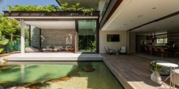 No projeto desta residência, com a assinatura da arquiteta Patricia Penna, a piscina lago se integra ao paisagismo de forma orgânica com suas bordas, pedras naturais e madeira. Atrás dele, o grande painel de vidro, com 7,20 m, se abre por completo, diluindo os limites entre o interior e o exterior| FOTO: Leandro Moraes