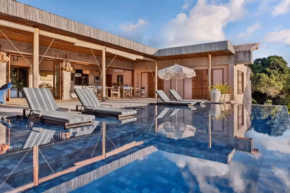 Casa Berimbau, na Bahia, se fecha para a rua e se abre para uma piscina que parece estar dentro e fora da sala ao mesmo tempo