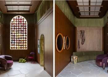 Dos dois ângulos do living é possível observar a composição do ambiente assinado pelo arquiteto Lucas Carrara. As estantes curvas com livros e objetos selecionados, o tecido verde drapeado entre as paredes revestidas de madeira e o teto, mobiliário e obras de arte se evidenciam em companhia do vitral com pratos de porcelana pintados à mão | Fotos: Felipe Cuine